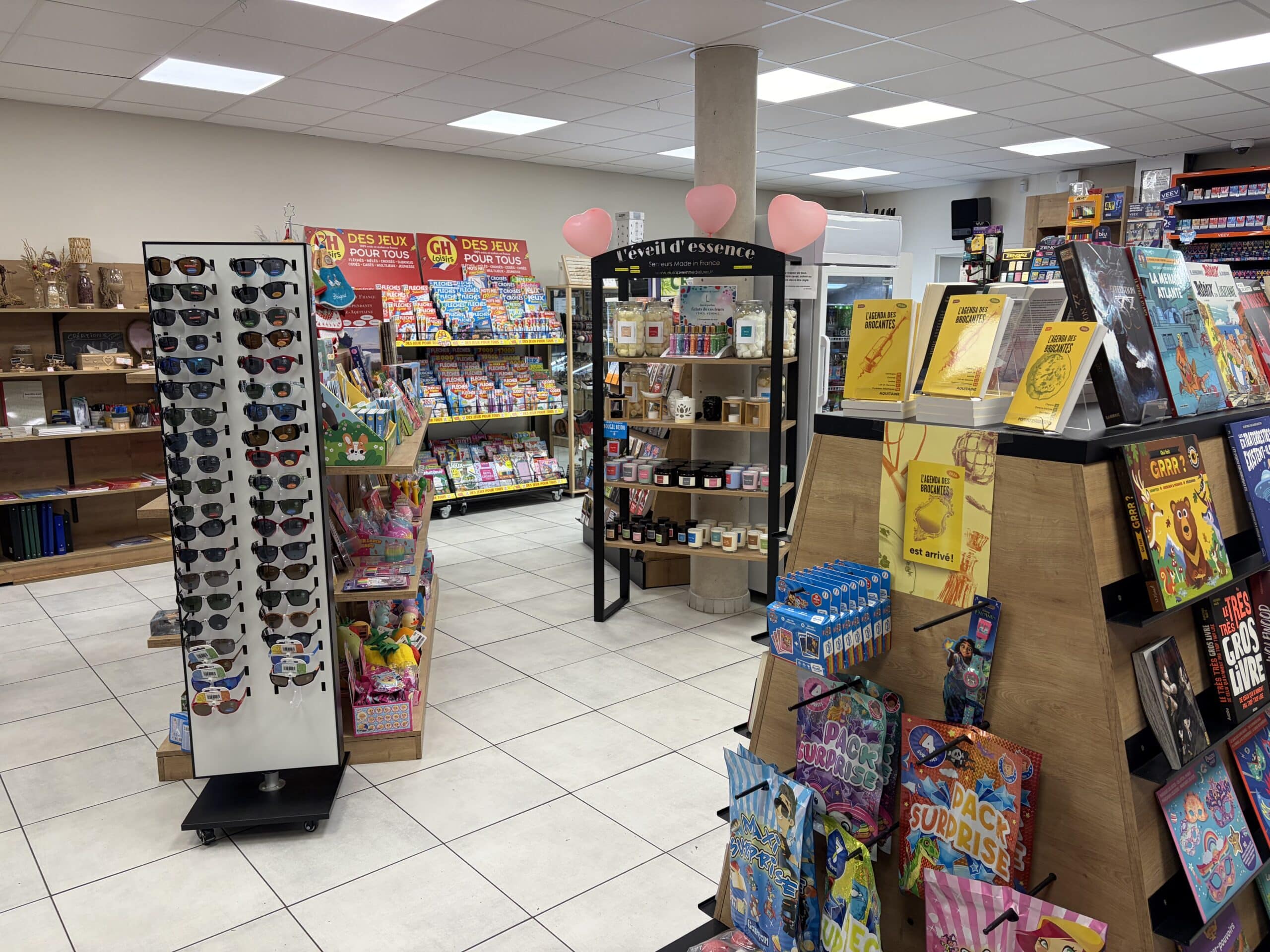 Rayonnage de presse et cadeaux avec présentoir de lunettes, magazines de jeux GH et bougies artisanales L'éveil d'essence.