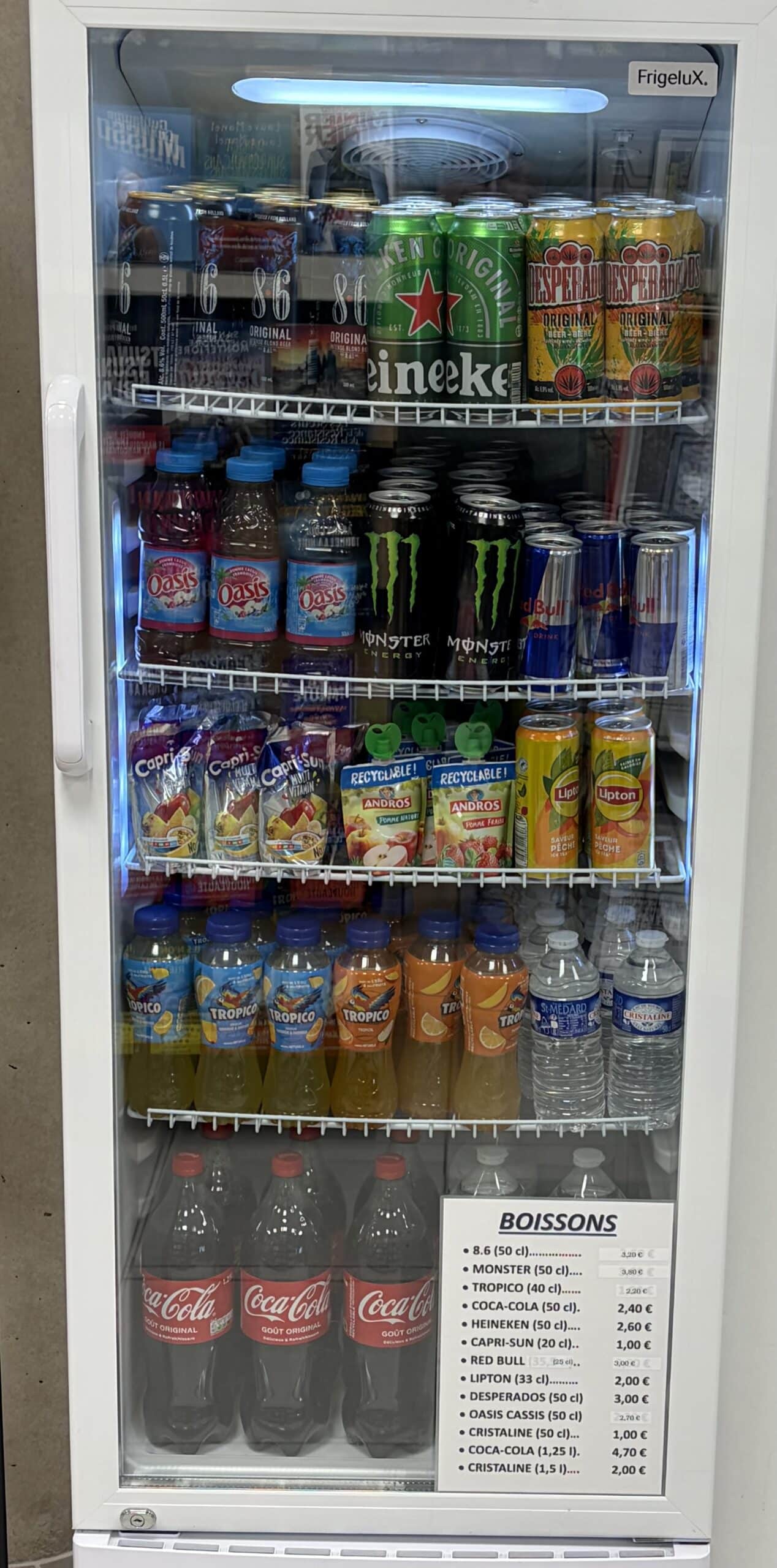 Intérieur d'un frigo Frigelux avec bières, sodas, jus et eaux, incluant une affiche tarifaire Boissons.
