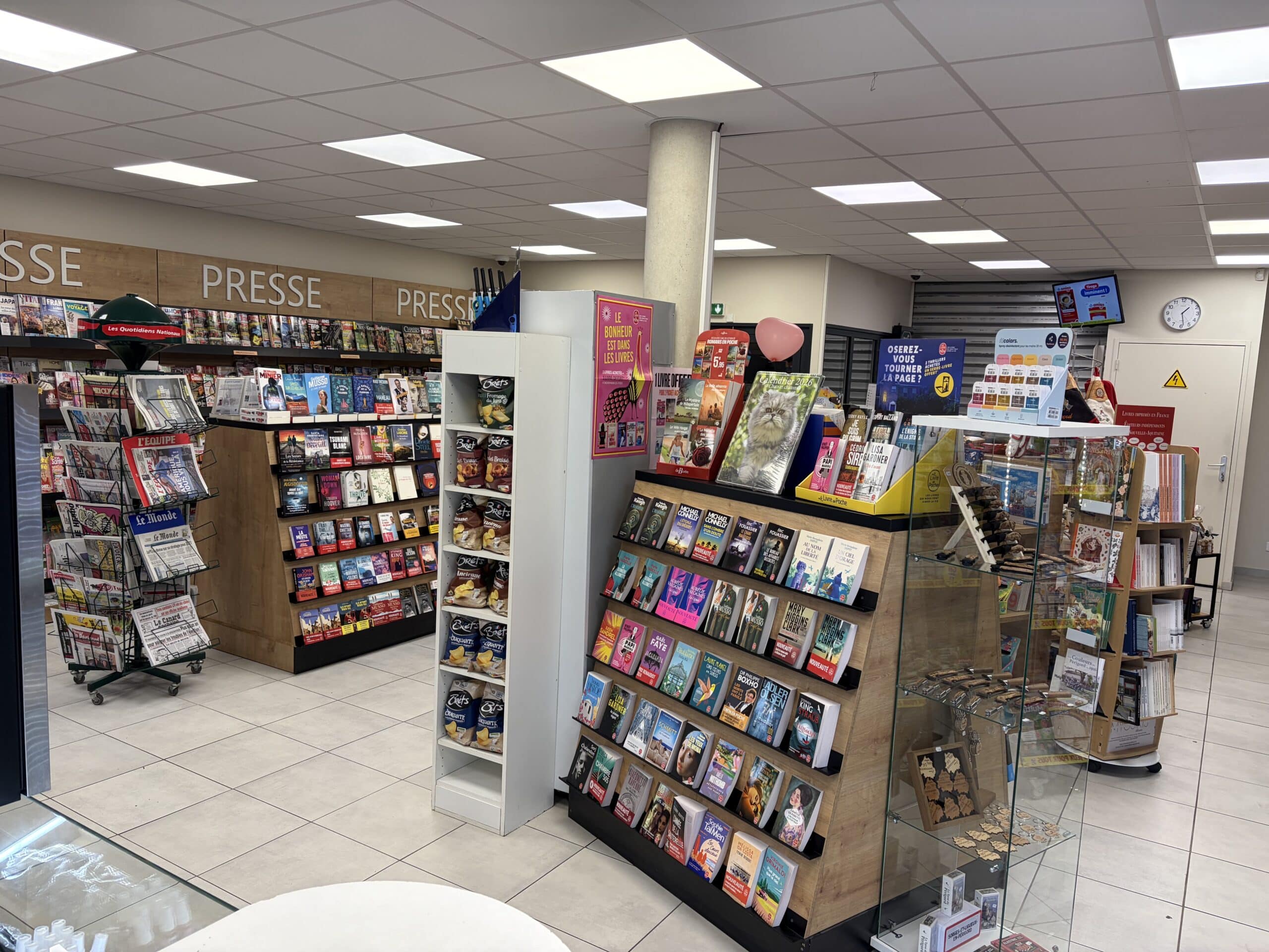 Rayonnages de presse et livres avec journaux Le Monde et romans en présentoir en bois dans une librairie moderne.