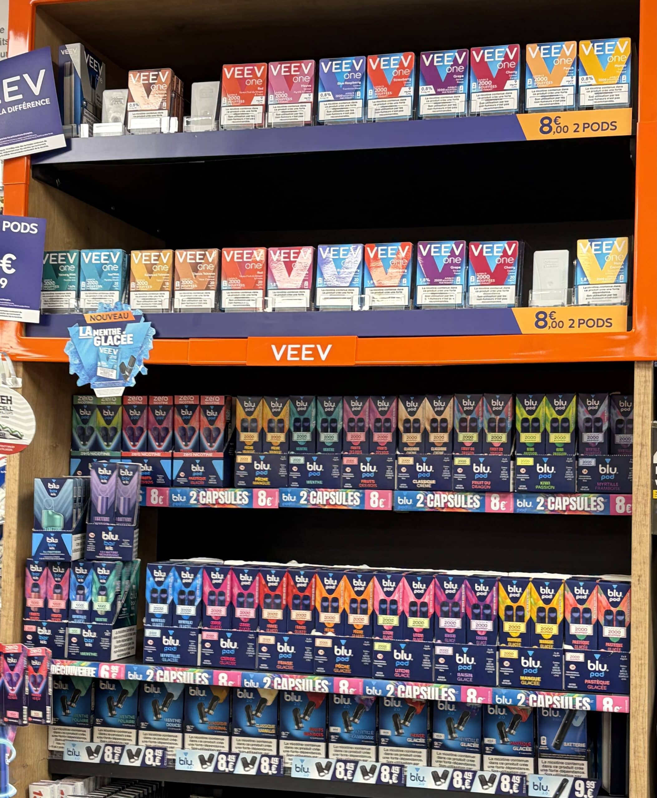 Rayonnage de capsules de vape VEEV one et blu pod avec saveurs menthe et fruits, prix affichés à 8€.
