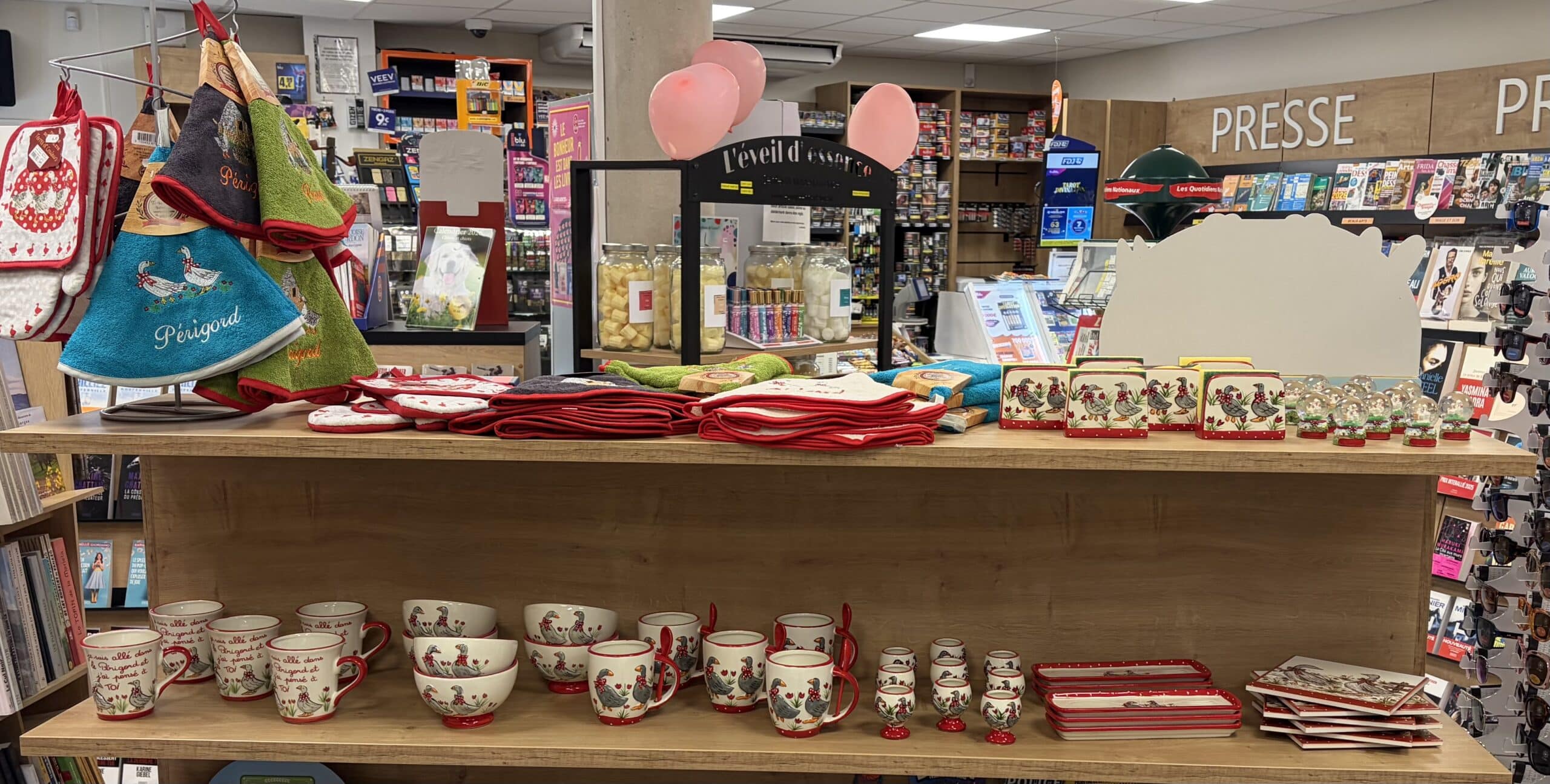 Rayon de souvenirs du Périgord : vaisselle, torchons à motifs d'oies et presse en arrière-plan.